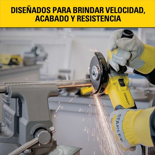 A person wearing protective gloves uses a yellow Stanley angle grinder to cut a metal pipe held in a vise, with sparks flying. The background shows a workshop, and there is a banner in Spanish that reads: 'Designed to provide speed, finish, and durability.'