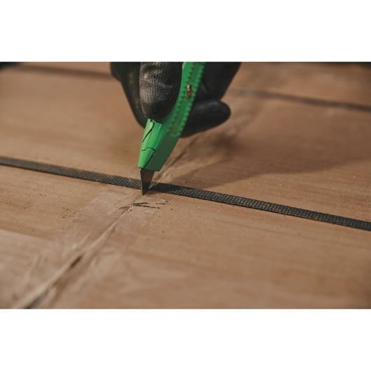 Photo of STANLEY 10-179 utility knife cutting cardboard box, close-up view of green handle and gloved hand.