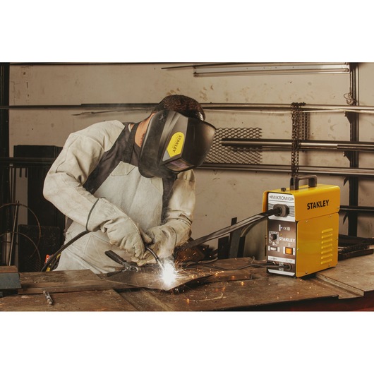Photo of STANLEY 10880 welding machine in use, with person welding metal on a workbench, sparks visible.
