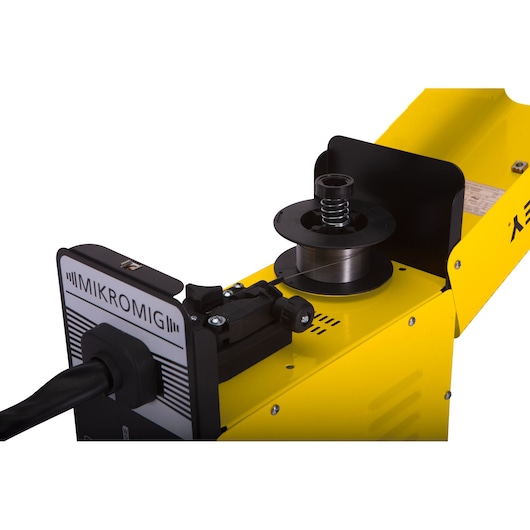 STANLEY 10880 MIG welder close-up showing wire feed mechanism, yellow body, and spool from side angle.