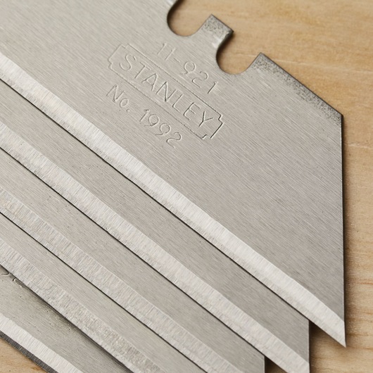Photo of STANLEY 11-921 utility blades stacked on a wooden surface, showing sharp metal edges.