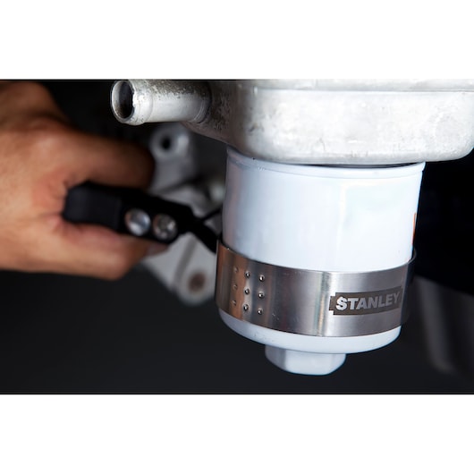 Close-up of STANLEY 78-228 oil filter wrench gripping a white oil filter, hand holding handle.