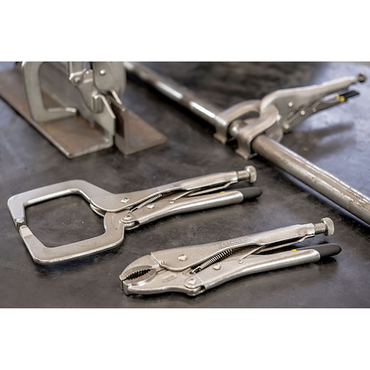 STANLEY 84-399 locking pliers and C-clamp pliers on a workbench, silver finish with black grip handles.