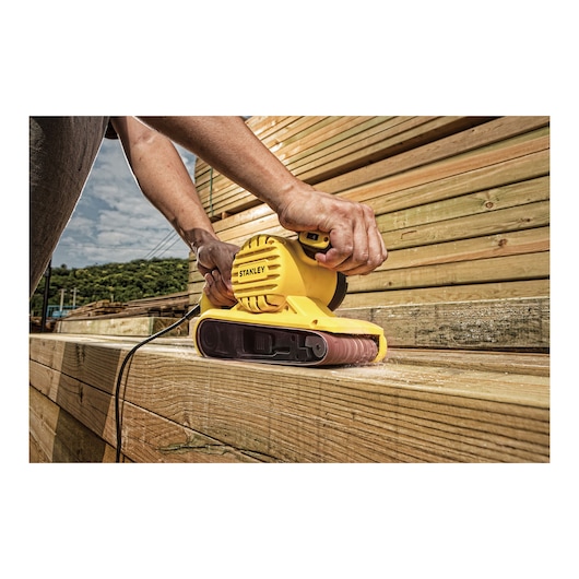 Stanley SB90-B2C yellow belt sander used on wooden planks outdoors, close-up photography.