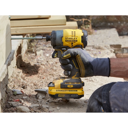 Stanley SKU SBI810D2K-B3 impact driver in use outdoors, yellow and black, held by gloved hand.