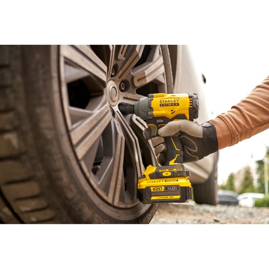 Stanley SBW920 photography of a yellow V20 FATMAX impact wrench being used on a car wheel outdoors.