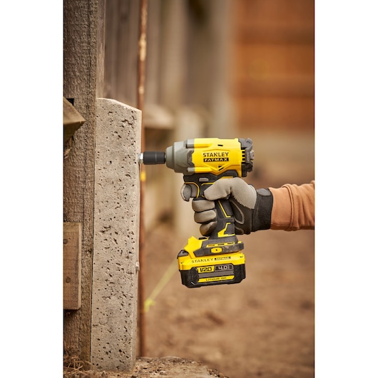 Stanley SBW920 impact driver held against concrete, yellow and black FATMAX cordless tool in outdoor setting.