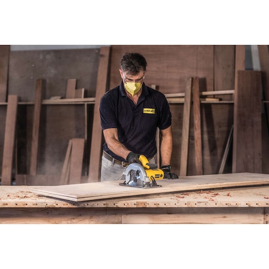 STANLEY SC16 circular saw in use cutting wood, worn by worker in workshop, product category photography.