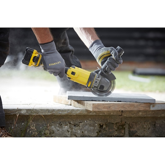 STANLEY SCG400M2K-KR cordless angle grinder cutting a tile outdoors, worker wearing gloves.