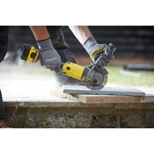 Photo of STANLEY SCG400 cordless angle grinder cutting a concrete slab outdoors, held by gloved hands.