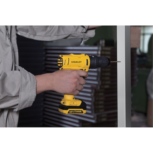 Stanley SCH121S2K-B2 cordless drill in use, yellow body, 12V lithium battery, side angle, power tool.