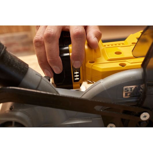 STANLEY SCM701-B3 battery-powered saw, close-up of yellow body and hand inserting battery.