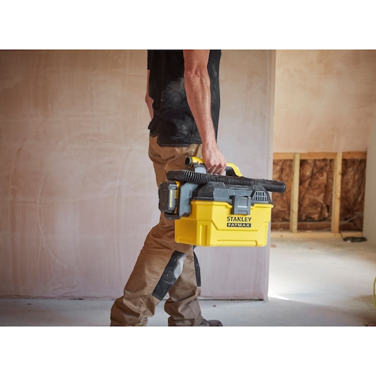 Photo of STANLEY SCV002 portable yellow vacuum being carried by a person at a jobsite.