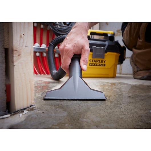 Stanley SCV002 wet vacuum in use, close-up of nozzle cleaning water from concrete floor, yellow unit in background