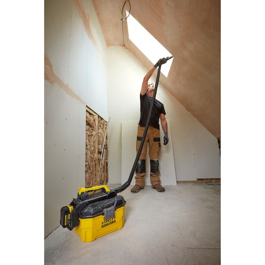 Stanley SCV002 vacuum cleaner in use during attic renovation, yellow body, flexible hose, jobsite setting.