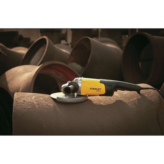 STANLEY SL227-B3 angle grinder with yellow and black body resting on a rusted metal pipe in an industrial setting.