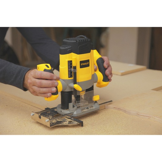 Photo of STANLEY SRR1200-AR plunge router in use on wood, yellow and black design, handled by a person.