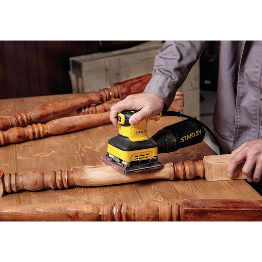 Stanley SS24-B3 sander used on a wooden table leg, close-up in workshop setting.