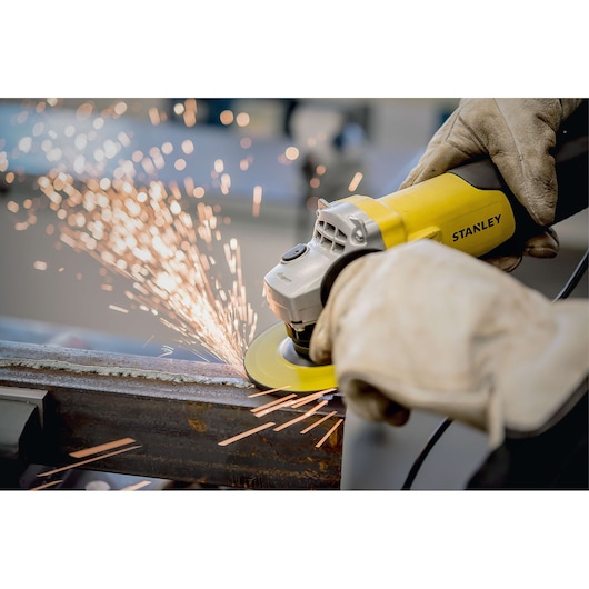 Photo of STANLEY STA0413 angle grinder in use, grinding metal with visible sparks, operated by gloved hands.