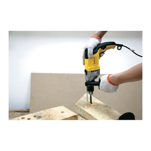 STANLEY STDH8013 photography of yellow corded drill in use drilling wood.