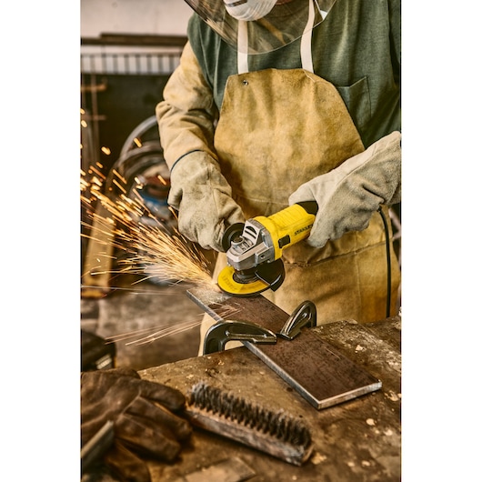 Stanley stgs9115 angle grinder in use, worker cutting metal with safety gear, workshop setting.