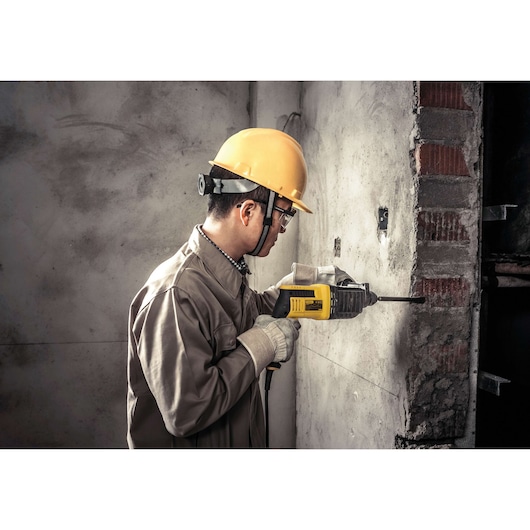 STANLEY STHR202K rotary hammer drill in use on concrete wall, side view, construction worker with safety gear.