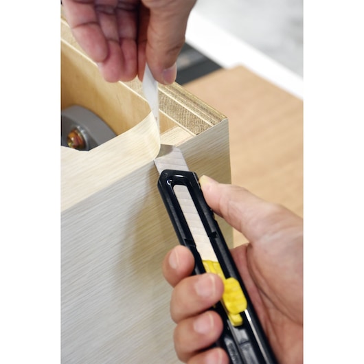 STANLEY STHT10323 utility knife cutting edge banding on wood panel, close-up photo.