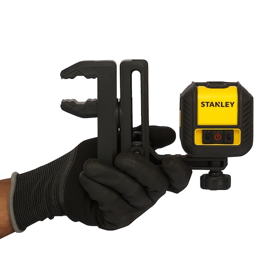 Photo of STANLEY STHT77498 laser level with mounting clamp held in a gloved hand, side angle.