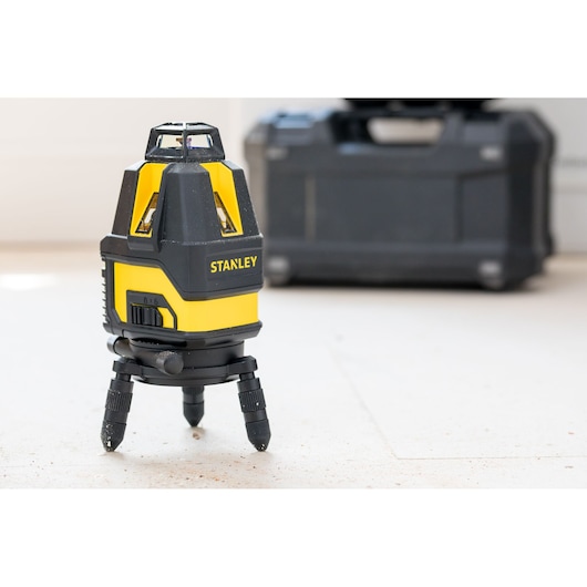 STANLEY STHT77521 laser level tool in yellow and black, front angle, with carrying case in background.