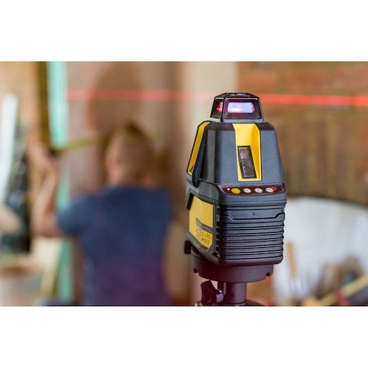 STANLEY STHT77521 laser level tool on tripod, projecting red horizontal line, workshop background.