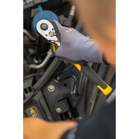 Photo of STANLEY STMT82665-0 ratchet wrench in use, black and yellow handle, held by gloved hand near engine.