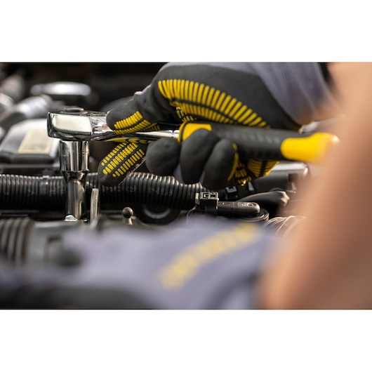 STANLEY STMT82665-0 ratchet wrench in use by a gloved hand on automotive engine, close-up photo.