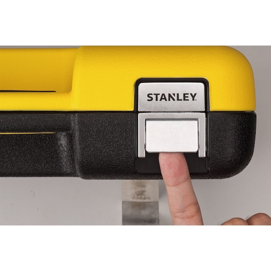 Stanley STMT82780 toolbox front latch, close-up, with a finger pressing the metal release on yellow and black case