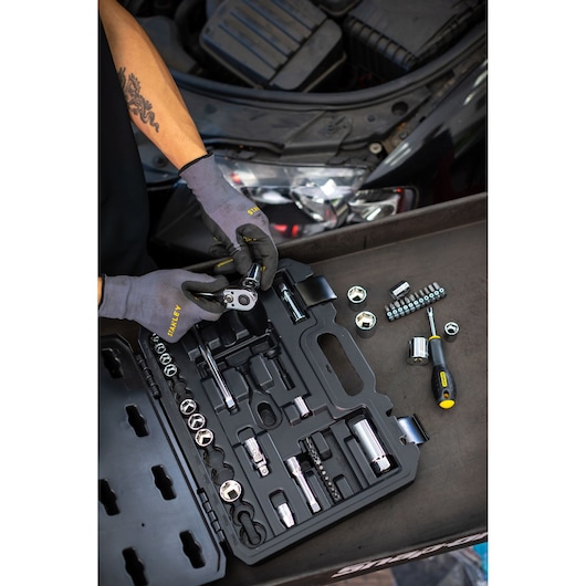 STANLEY STMT82829-1 socket set with ratchet and screwdriver, displayed open by mechanic near car engine.