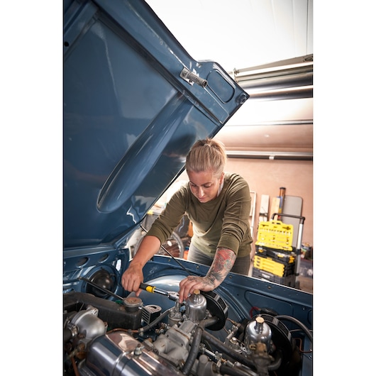 Stanley STMT82832-LA ratchet wrench used on car engine, person working in garage, side angle photo.