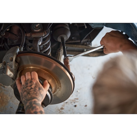 Photo of a person using a STANLEY STMT82832-LA wrench to work on a car's brake assembly.