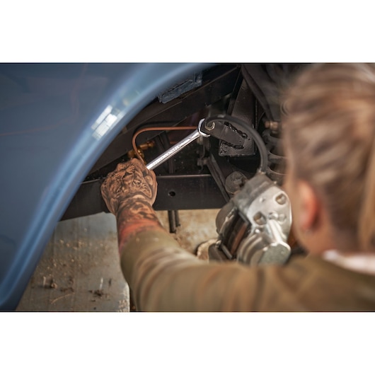 STANLEY STMT82832-LA combination wrench being used to repair a vehicle part in a workshop setting.
