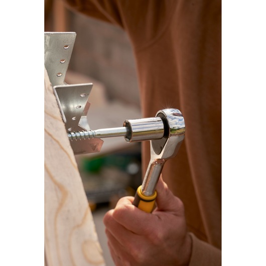 STANLEY STMT82832-LA ratchet wrench in use tightening metal bracket screw, close-up photo.