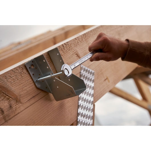 STANLEY STMT82832-LA wrench tightening bolt on metal bracket attached to wooden beam, construction site setting.