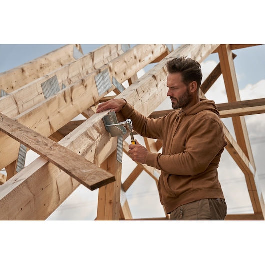 STANLEY STMT82832-LA hammer in use by worker assembling wooden roof frame outdoors.