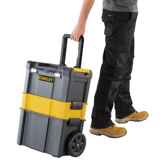 Stanley rolling toolbox, gray and yellow, front angle, pulled by person wearing work pants and boots