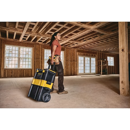 STANLEY STST18631 rolling tool box with yellow and black design in a construction site, pulled by a worker.