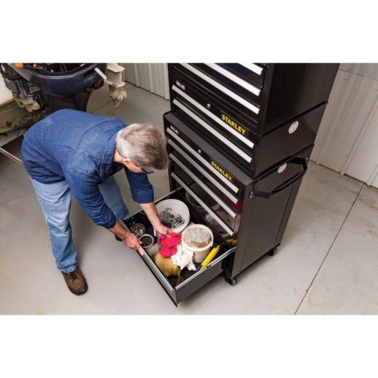 Stanley STST22753BK tool chest with open drawer, man organizing tools and accessories in a garage setting.