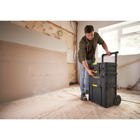 STANLEY STST83319-1 rolling black tool chest stack with yellow latches in a renovation room, person accessing top box.