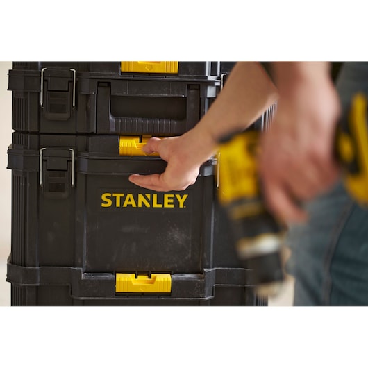 Photo of STANLEY STST83319-1 stackable tool boxes with yellow latches, person holding drill in front.
