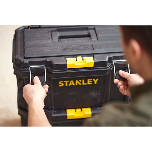 Photo of STANLEY STST83319-1 black tool box with yellow latches, hands unlocking front metal clips.