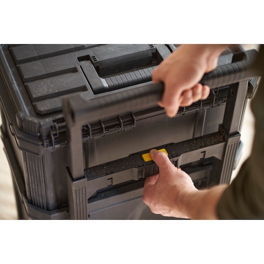 STANLEY STST83319-1 tool chest close-up, hand pressing yellow button, black plastic, top angle.