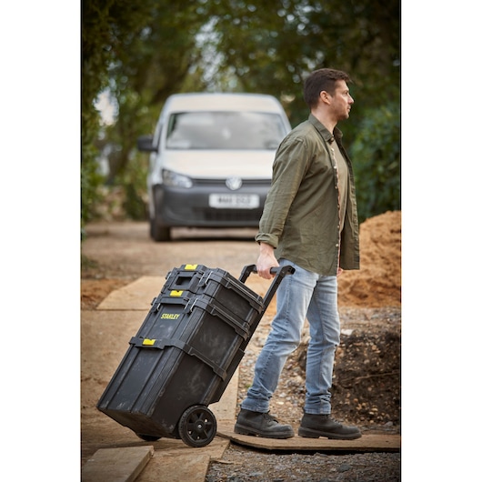 Stanley STST83319-1 rolling toolbox with black body and yellow latches, shown being pulled by user outdoors.
