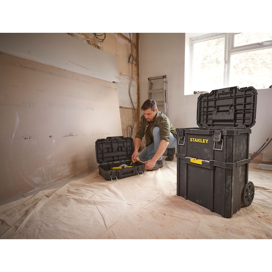 STANLEY STST83319-1 rolling toolbox in black, open lid, used in a workshop setting with tools inside.