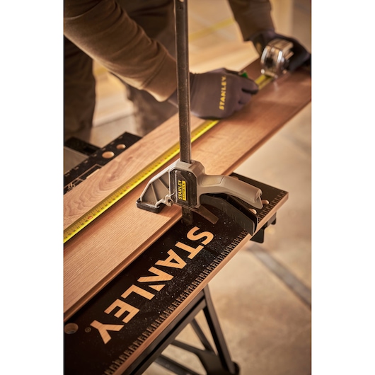 STANLEY STST83400-1 clamp holding wood on black workbench with tape measure, close-up angle.
